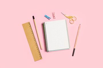 Un cuaderno junto a lápices, una tijera con forma de cigueña y una regla sobre un fondo rosa pastel liso y aislado. Vista superior y de cerca. Copy space