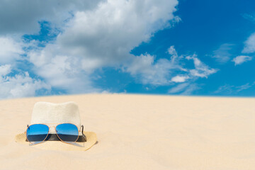 Blue sunglasses and a light hat lie on the sand against the blue sky. Summer vacation, travel and tourism concept