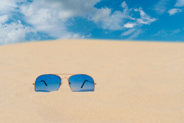 Blue sunglasses lie on the sand against the blue sky. Summer vacation, travel and tourism concept