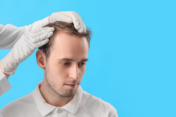Doctor examining young man's hair on blue background, closeup