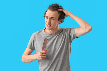 Upset young man with comb losing hair on blue background
