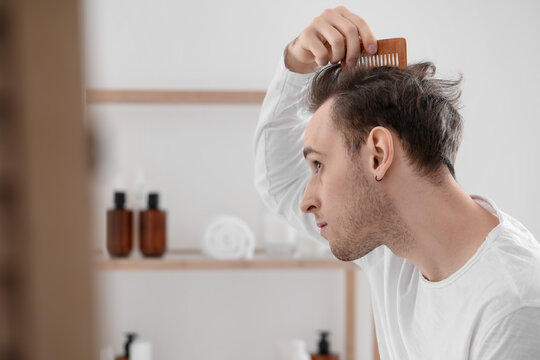 Young Man Combing Hair Near Mirror In Bathroom