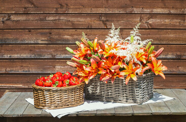 Wicker baskets with fresh strawberry and orange lilies and white astilbe flowers on wooden table.