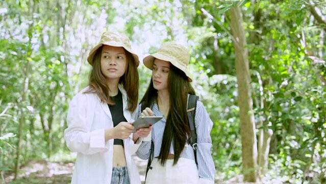 Two Asian teenage girls are best friends, open tablet in hand view nature walk map this forest, which is open for people come play, they are looking at walking map here thinking which way walk.