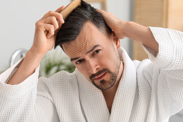 Worried young man combing hair in bathroom, closeup