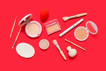 Fototapeta na wymiar Decorative cosmetics with makeup brushes and sponges on red background