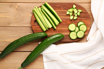 Board with cut and whole cucumbers on wooden background