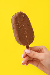 Woman holding delicious chocolate covered ice cream on stick against yellow background