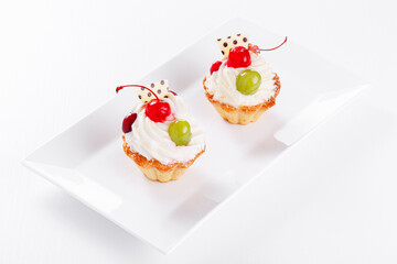 Beautiful cream cakes with cherries and grapes on a plate on a white background