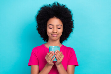 Photo of satisfied adorable girl with afro chevelure wear pink t-shirt hands holding cup of cacao isolated on blue color background