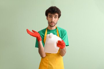 Confused young man with bottle of detergent on green background