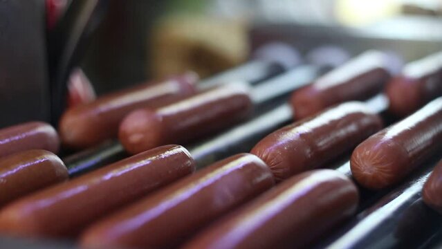 Long sausages rotates on the roller grill for cooking a hot dog