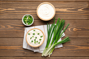 Bowls of tasty sour cream with green onion on wooden background