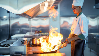 Chef in restaurant kitchen at stove and pan cooking flambe on food