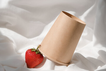 Disposable paper cup. Strawberry. White tablecloth. Sunlight. Biodegradable tableware. Copy space.