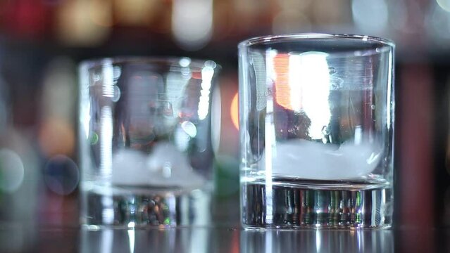 Bartender pours whiskey with ice in two glasses