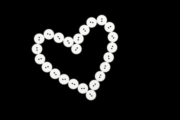 Heart from white buttons on a black background. Symbol of love