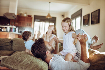 Obraz premium Young family playing together on the couch in the living room at home