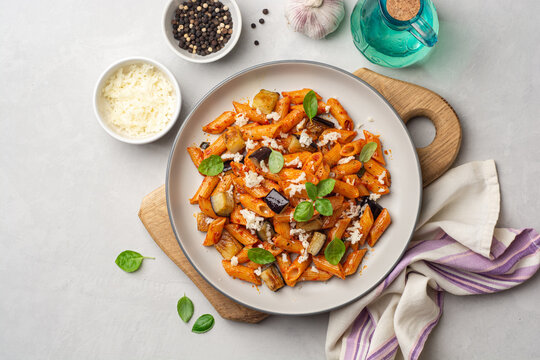 Pasta alla Norma. Traditional Italian dish with eggplant, tomato sauce, ricotta cheese and basil in plate on concrete background
