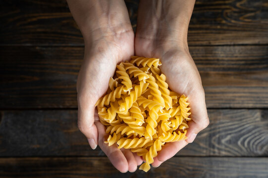 Raw uncooked Italian pasta fusilli held in two hands over a dark wooden background