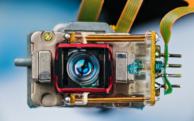 Closeup a small lens of optical read-write head with connection of electronic flex cables. Laser pickup with copper winding, permanent neodymium magnets and coil springs. Part of an CD-DVD disc drive. © KPixMining