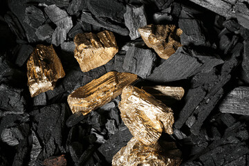 Golden nuggets on black charcoal, closeup