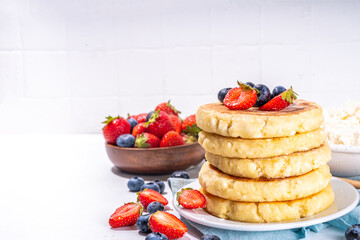 Sweet homemade cottage cheese pancakes, american version of syrniki or cottage cheese fritters, big pan fried cheesy pancakes with fresh summer blueberry and strawberry, healthy high-protein breakfast