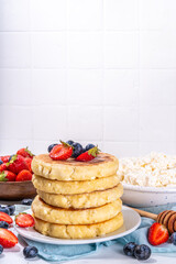 Sweet homemade cottage cheese pancakes, american version of syrniki or cottage cheese fritters, big pan fried cheesy pancakes with fresh summer blueberry and strawberry, healthy high-protein breakfast