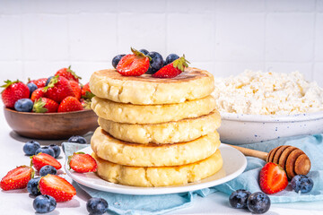 Sweet homemade cottage cheese pancakes, american version of syrniki or cottage cheese fritters, big pan fried cheesy pancakes with fresh summer blueberry and strawberry, healthy high-protein breakfast