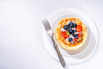 Sweet homemade cottage cheese pancakes, american version of syrniki or cottage cheese fritters, big pan fried cheesy pancakes with fresh summer blueberry and strawberry, healthy high-protein breakfast