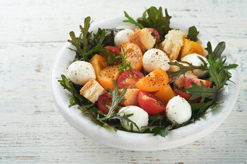 Tuscan Panzanella. Cherry Tomatoes salad with arugula, basil, mozzarella and bread crackers on white bowl. Traditional italian salad. Mediterranean healthy food and cuisine.