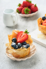 Phyllo or filo pies with fresh berries strawberries and blueberries, cheese filling topped with fresh mint on white plate. Homemade Filo pastry paskets. Delicious filo pastry dessert.