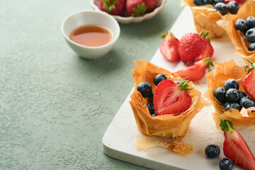 Phyllo or filo pies with fresh berries strawberries and blueberries, cheese filling topped with fresh mint on white plate. Homemade Filo pastry paskets. Delicious filo pastry dessert.