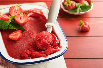 Strawberry granita or fresh berry sorbet in white rustic bowl on old wooden table background. Ice cream with strawberry and mint. Summer treat. Top view.