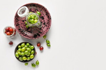 Bowl and jars with fresh gooseberries on white background