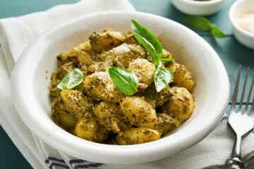 Potato gnocchi. Traditional homemade potato gnocchi with sauce pesto, kitchen table and basil on old rustic turquoise kitchen table. Traditional Italian food. Top view.