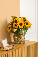 Vase with beautiful sunflowers on wooden cabinet near beige wall