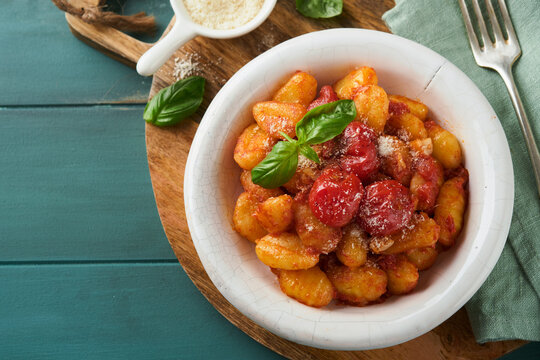 Potato gnocchi. Traditional homemade potato gnocchi with tomato sauce, basil and parmesan cheese on turquoise rustic kitchen table background. Traditional Italian food. Top view.