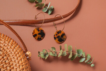 Wicker bag with beautiful earrings and eucalyptus branches on color background