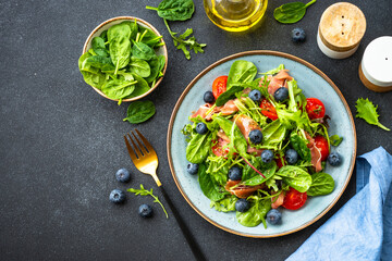 Healthy salad with green leaves, tomatoes and jamon on black.