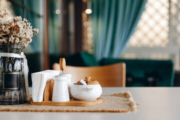 pepper and sauce, a wooden napkin holder with white napkins, a glass vase with dry flowers on the background of a summer veranda room