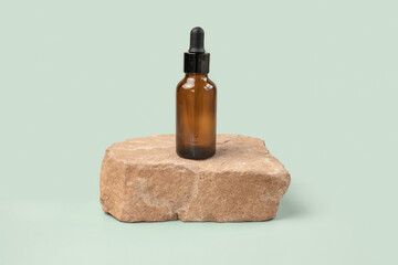 Dark amber glass bottle standing on stone. Natural skin care SPA beauty product design. Mineral organic oil cosmetics. Green background. MockUp. Oily pipette. Face and body treatment. Front view stand