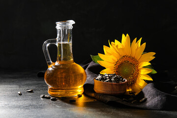 Decanter of sunflower oil and wooden bowl with seeds on black background