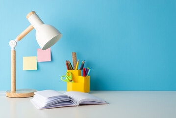 Organized school setup: side view photo of a desk with stationery holder, open book, and a lamp....