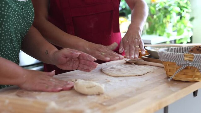 closeup of the hands of two women with their aprons kneading dough in the kitchen. reparing some dessert