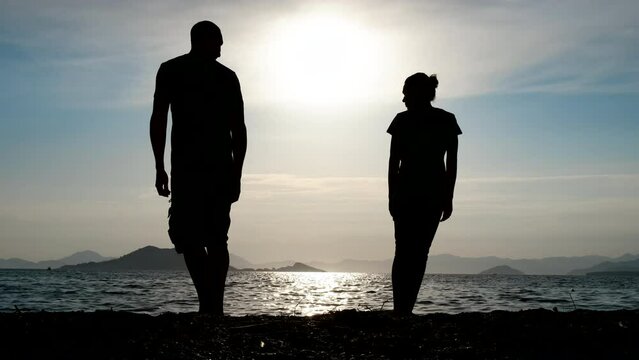Misunderstanding in a couple. Silhouette of a couple in love standing with their backs to each other on the sea beach.