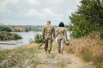 A man and a woman in the military uniform of Ukraine walk along the path and hold hands.