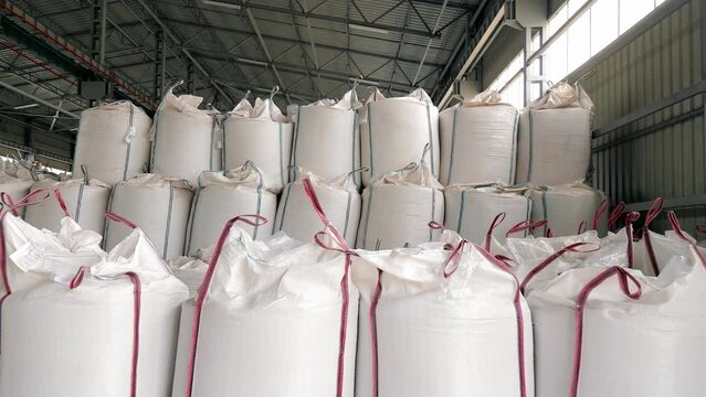 White bags for storing grain crops in the Warehouse. Storage of corn and soybeans in the warehouse. Large industrial bags for heavy loads. Warehouse with Bulk Bag.