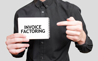 Businessman holding a white notepad with text INVOICE FACTORING, business concept