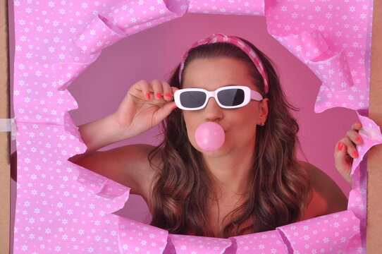 jovem mulher da moda retr&ocirc; fazendo bolha com chiclete em fundo rosa 
